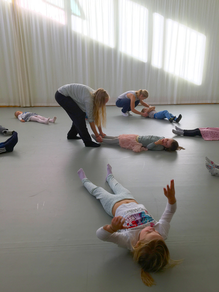 PPU-student Tuva Hennum drar barna bortover gulvet mens de ligger rolig. Vilde Halle Ekeland i bakgrunnen hjelper femåringene å slappe av.  