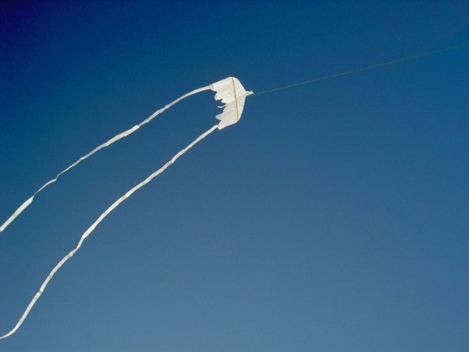 Image: Truls Corneliussen. Photograph of a small kite by Kari Carlsen, made from three cigarette papers against a blue sky.
Image: Truls Corneliussen. Photograph of a small kite by Kari Carlsen, made from three cigarette papers against a blue sky.